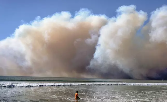 A swimmer watches as a large dark plume of smoke passes over the beach from a wildfire from Pacific Palisades, in Santa Monica, Calif., Tuesday, Jan. 7, 2025. (AP Photo/Richard Vogel)