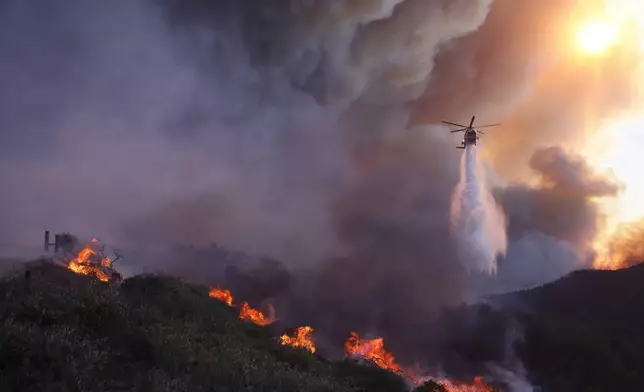 Water is dropped by helicopter on the advancing Palisades Fire in the Pacific Palisades neighborhood of Los Angeles, Tuesday, Jan. 7, 2025. (AP Photo/Etienne Laurent)