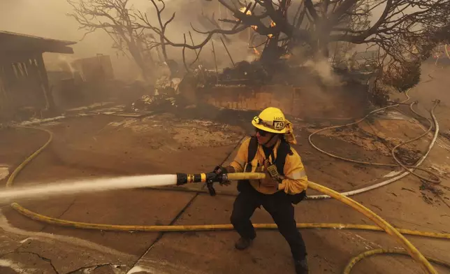 A firefighter hoses down flames from the Palisades Fire in front of a residence in the Pacific Palisades neighborhood of Los Angeles, Tuesday, Jan. 7, 2025. (AP Photo/Ethan Swope)