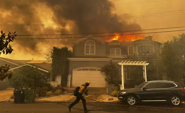 A residence burns as a firefighter battles the Palisades Fire in the Pacific Palisades neighborhood of Los Angeles Tuesday, Jan. 7, 2025. (AP Photo/Eugene Garcia)