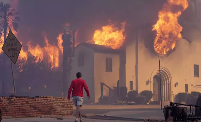 A man walks in front of the burning Altadena Community Church, Wednesday, Jan. 8, 2025, in the downtown Altadena section of Pasadena, Calif. (AP Photo/Chris Pizzello)