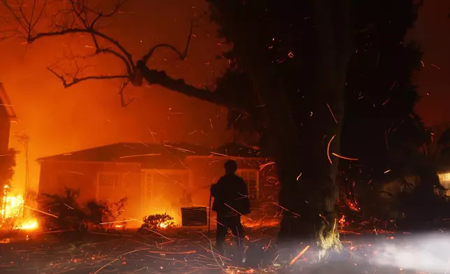 A person tries to hose down embers from the Palisades Fire in the Pacific Palisades neighborhood of Los Angeles, Tuesday, Jan. 7, 2025. (AP Photo/Etienne Laurent)