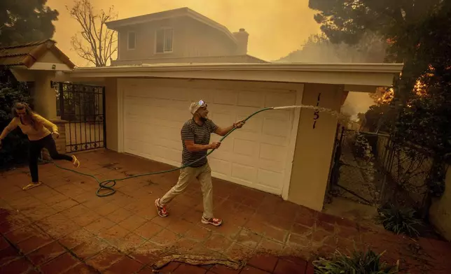 Will Adams uses a garden hose to keep flames from damaging his home as the Palisades Fire advances in the Pacific Palisades neighborhood of Los Angeles, Tuesday, Jan. 7, 2025. (AP Photo/Ethan Swope)