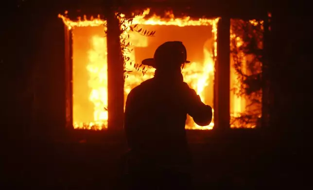 A firefighter is silhouetted in front of a burning structure as the Palisades Fire sweeps through in the Pacific Palisades neighborhood of Los Angeles, Tuesday, Jan. 7, 2025. (AP Photo/Etienne Laurent)