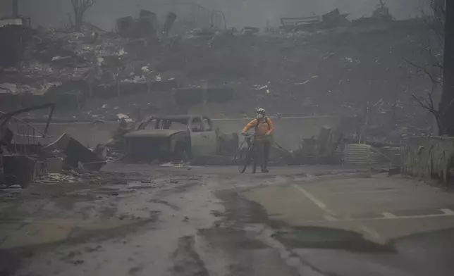 A person bikes through a burned out area as the Palisades Fire ravages a neighborhood amid high winds in the Pacific Palisades neighborhood of Los Angeles, Wednesday, Jan. 8, 2025. (AP Photo/Damian Dovarganes)