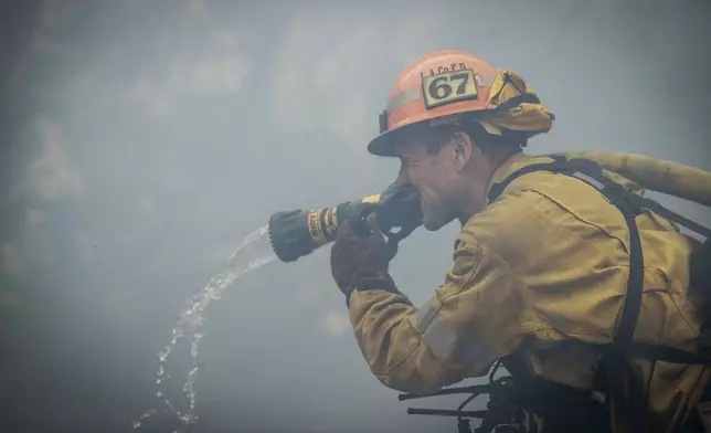 A firefighters make a stand in front of the advancing Palisades Fire in the Pacific Palisades neighborhood of Los Angeles, Tuesday, Jan. 7, 2025. (AP Photo/Ethan Swope)