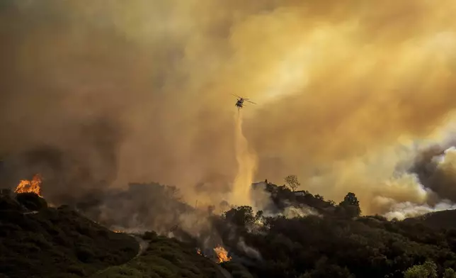 Water is dropped on the advancing Palisades Fire by helicopter in the Pacific Palisades neighborhood of Los Angeles, Tuesday, Jan. 7, 2025. (AP Photo/Ethan Swope)