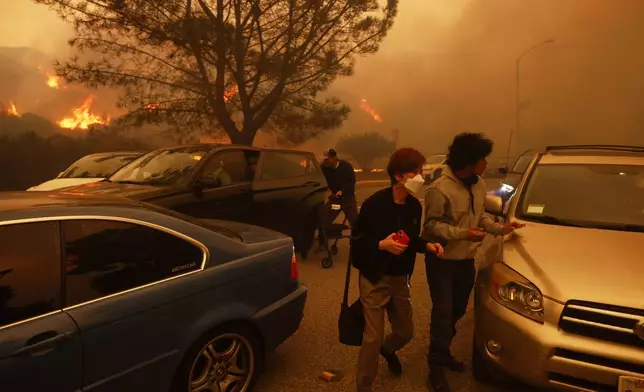 People flee from the advancing Palisades Fire, by car and on foot, in the Pacific Palisades neighborhood of Los Angeles Tuesday, Jan. 7, 2025. (AP Photo/Etienne Laurent)