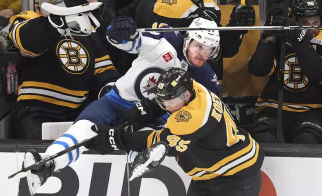 Winnipeg Jets defenseman Dylan Samberg, left, is checked into the Bruins bench by Boston Bruins left wing Cole Koepke (45) during the second period of an NHL hockey game, Thursday, Jan. 30, 2025, in Boston. (AP Photo/Charles Krupa)