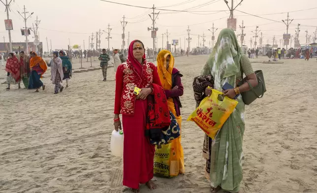 Hindu women wait to join their family members after bathing at the confluence of the Ganges, the Yamuna and the mythical Saraswati rivers, a day before the official beginning of the 45-day-long Maha Kumbh festival, in Prayagraj, India, Sunday, Jan. 12, 2025. (AP Photo/Ashwini Bhatia)