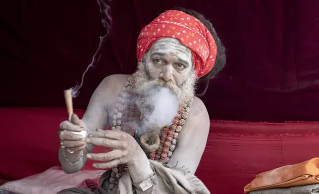 A Hindu holy man smokes marijuana at his makeshift living quarters at the confluence of the Ganges, the Yamuna and the mythical Saraswati rivers, a day before the official beginning of the 45-day-long Maha Kumbh festival, in Prayagraj, India, Sunday, Jan. 12, 2025. (AP Photo/Ashwini Bhatia)