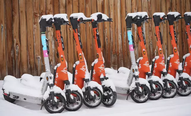Electric scooters covered in snow sit idle along Galapago Street as a winter storm sweeps over the intermountain West, plunging temperatures into the single digits and bringing along a light snow in its wake Saturday, Jan. 18, 2025, in Denver. (AP Photo/David Zalubowski)