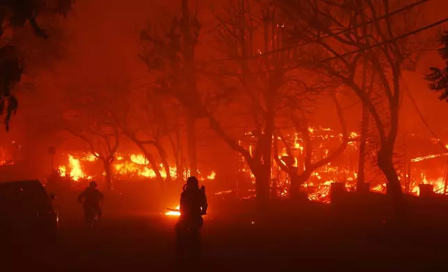 Two persons ride by on motorcycles as the Palisades Fire destroys a neigbhborhood in the Pacific Palisades neighborhood of Los Angeles, Tuesday, Jan. 7, 2025. (AP Photo/Etienne Laurent)