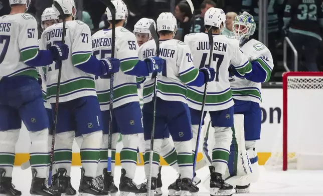 Vancouver Canucks goaltender Kevin Lankinen, far right, is greeted by teammates, including defenseman Noah Juulsen (47) as they celebrate a 4-3 win in a shootout over the Seattle Kraken in an NHL hockey game Thursday, Jan. 2, 2025, in Seattle. (AP Photo/Lindsey Wasson)