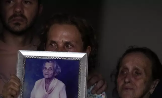 Euripedes Vaz, center, is emotional as she holds the photo of her dead mother next to her sister Maria Vaz, right, and her son, while singing hymns in honor of the Holy Kings during a procession marking Epiphany, or Three Kings Day, in Santo Antonio de Goias, Brazil, Saturday, Jan. 4, 2025. (AP Photo/Eraldo Peres)