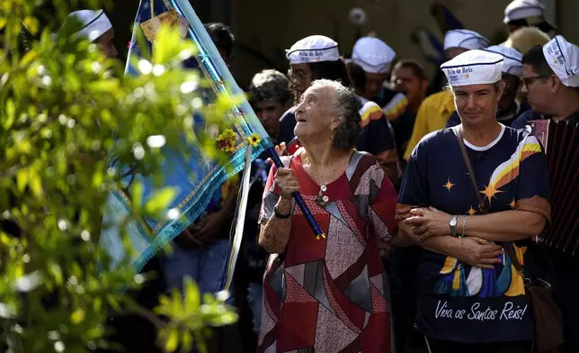 Matriarch Terezinha de Jesus, left, carries the flag of the Holy Kings next to Santo Antonio Folia de Reis group during a procession marking Epiphany, or Three Kings Day in Santo Antonio de Goias, Brazil, Saturday, Jan. 4, 2025. (AP Photo/Eraldo Peres)