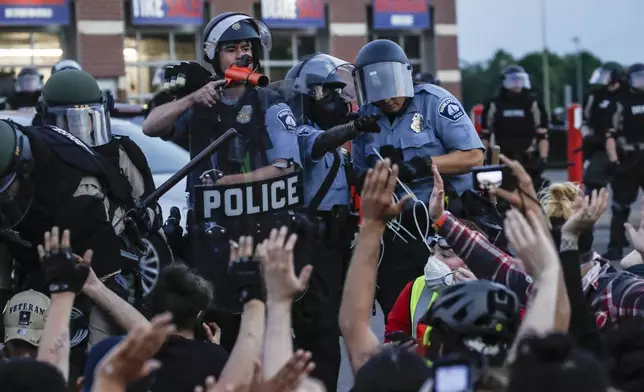 FILE - A police officer points a hand cannon at protesters who have been detained pending arrest on South Washington Street in Minneapolis, May 31, 2020, as protests continued following the death of George Floyd. (AP Photo/John Minchillo, File)