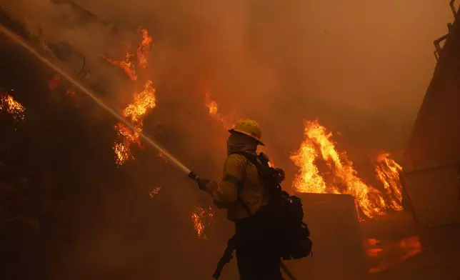 A firefighter battles the advancing Palisades Fire around a structure in the Pacific Palisades neighborhood of Los Angeles Tuesday, Jan. 7, 2025. (AP Photo/Etienne Laurent)