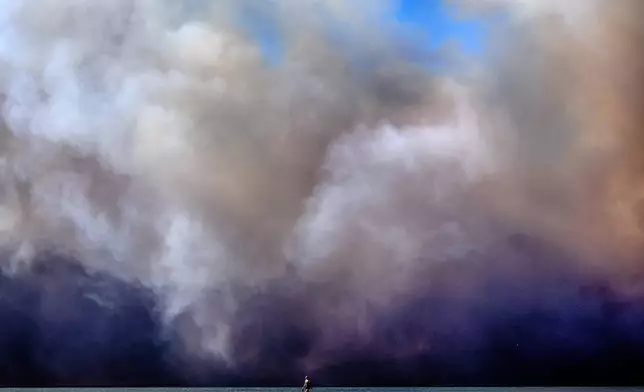 A lone beachgoer walks along the coast as a large dark plume of smoke passes over the beach from a wildfire from Pacific Palisades, from Santa Monica, Calif. on Tuesday, Jan. 7, 2025. (AP Photo/Richard Vogel)