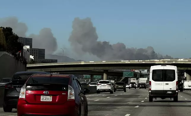 Smoke from a brush fire in the Pacific Palisades rises over the 405 freeway in Los Angeles on Tuesday, Jan. 7, 2025. (AP Photo/Ethan Swope)