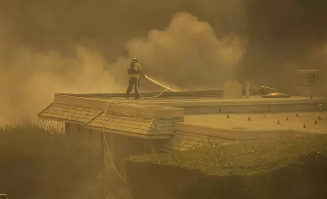 A firefighter tries to contain the Palisades Fire from a rooftop in the Pacific Palisades neighborhood of Los Angeles, Tuesday, Jan. 7, 2025. (AP Photo/Ethan Swope)