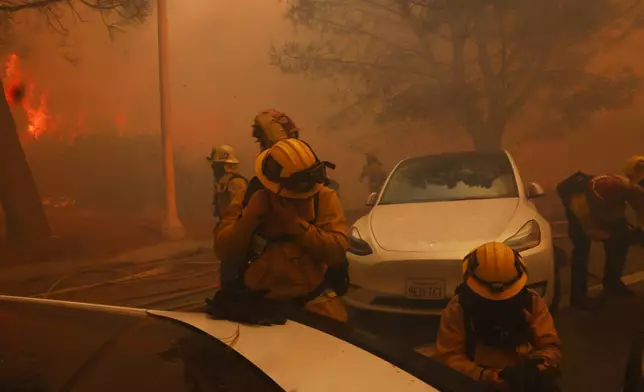 Firefighters try to protect themselves from flying embers from the Palisades Fire in the Pacific Palisades neighborhood of Los Angeles, Tuesday, Jan. 7, 2025. (AP Photo/Etienne Laurent)