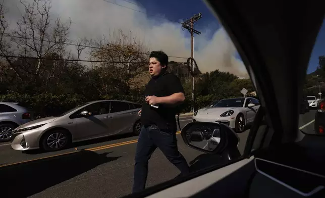 A person flees from an advancing wildfire in the Pacific Palisades neighborhood of Los Angeles Tuesday, Jan. 7, 2025. (AP Photo/Ethan Swope)