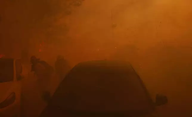 A pair of firefighters try to protect themselves from flying embers from the Palisades Fire in the Pacific Palisades neighborhood of Los Angeles Tuesday, Jan. 7, 2025. (AP Photo/Etienne Laurent)