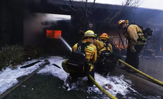 Firefighters battle the advancing Palisades Fire as it damages a residence in the Pacific Palisades neighborhood of Los Angeles, Tuesday, Jan. 7, 2025. (AP Photo/Ethan Swope)