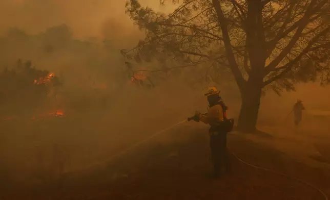 A firefighter battles the advancing Palisades Fire in the Pacific Palisades neighborhood of Los Angeles, Tuesday, Jan. 7, 2025. (AP Photo/Etienne Laurent)