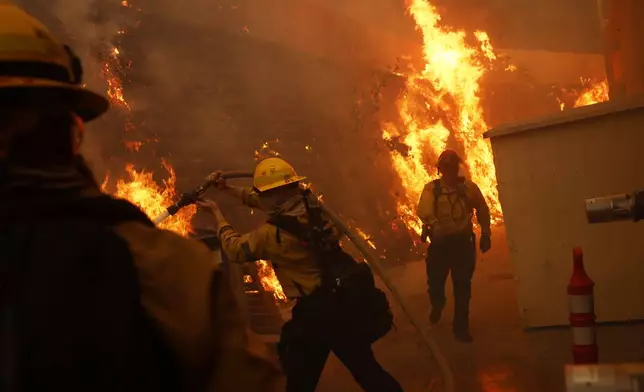 Firefighters protect structures from the advancing Palisades Fire in the Pacific Palisades neighborhood of Los Angeles, Tuesday, Jan. 7, 2025. (AP Photo/Etienne Laurent)