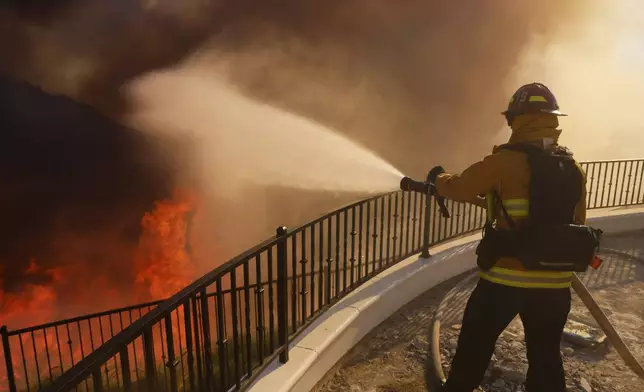 A firefighter makes a stand in front of the advancing Palisades Fire in the Pacific Palisades neighborhood of Los Angeles, Tuesday, Jan. 7, 2025. (AP Photo/Etienne Laurent)