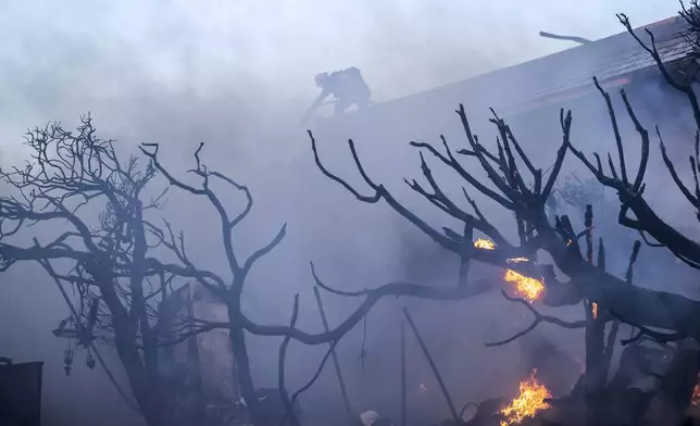 A firefighter tries to contain the Palisades Fire from a rooftop in the Pacific Palisades neighborhood of Los Angeles, Tuesday, Jan. 7, 2025. (AP Photo/Ethan Swope)