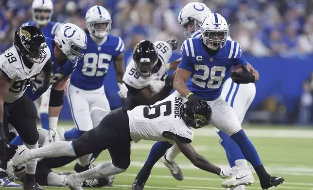 Indianapolis Colts running back Jonathan Taylor (28) runs with the ball as Jacksonville Jaguars safety Darnell Savage (6) and defensive tackle Jeremiah Ledbetter (99) move in during the first half of an NFL football game, Sunday, Jan. 5, 2025, in Indianapolis. (AP Photo/Michael Conroy)