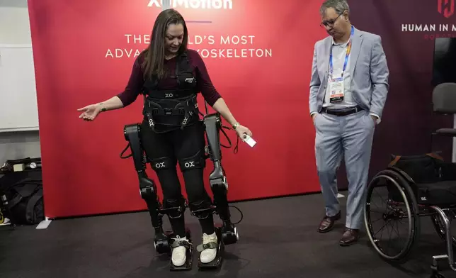 Chloe Angus, director of Lived Experience at Human in Motion Robotics and paraplegic, stands and moves with help from the XoMotion exoskeleton at the Human In Motion Robotics booth during the CES tech show Wednesday, Jan. 8, 2025, in Las Vegas. The wearable robotic exoskeleton is designed to assist patients with mobility impairments due to spinal cord injuries, stroke and other neurological conditions in standing up and walking. (AP Photo/John Locher)