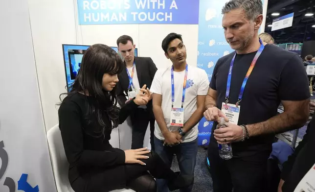 A Realbotix humanoid robot, left, speaks with attendees at a Realbotix booth during the CES tech show Wednesday, Jan. 8, 2025, in Las Vegas. (AP Photo/Abbie Parr)