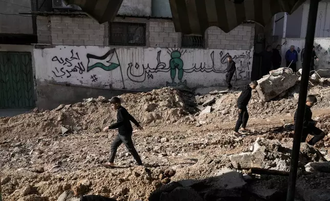 An Arabic mural reading, "Palestine," is the backdrop as Palestinian children walk on a street damaged in Israeli military operation at the Al-Fara'a refugee camp in the West Bank, Tuesday, Jan. 7, 2025. (AP Photo/Majdi Mohammed)