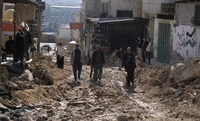 Palestinians walk on a street damaged in an Israeli military operation in the Al-Fara'a refugee camp in the West Bank, Tuesday, Jan. 7, 2025. (AP Photo/Majdi Mohammed)