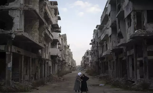 Women talk on a street surrounded by buildings that were destroyed during the civil war at the district of Khalidiya in Homs, Syria, Wednesday, Jan. 1, 2025. (AP Photo/Leo Correa)