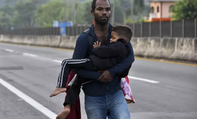 A migrant carries a child through Tapachula, Chiapas state, Mexico, Thursday, Jan. 2, 2025, as part of a caravan of migrants trying to reach the U.S. border. (AP Photo/Edgar H. Clemente)