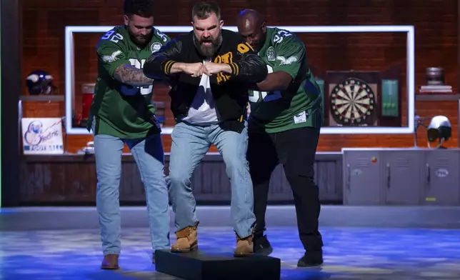 Former NFL player and ESPN analyst Jason Kelce, center, gets pushed out like an old electronic football player during the taping of "They Call It Late Night with Jason Kelce", Friday, Jan. 3, 2025, in Philadelphia. (AP Photo/Chris Szagola)