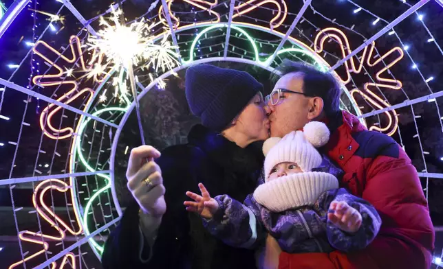 A couple kisses as they walk with their child in a square decorated for Christmas and the New Year festivities in Donetsk in Russian-controlled Donetsk region, eastern Ukraine, Tuesday, Dec. 31, 2024. (AP Photo/Alexei Alexandrov)