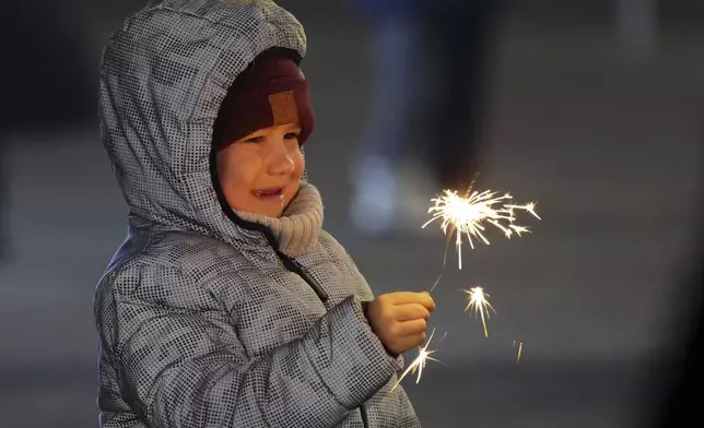 A girl holds a sparkler as she walks in a square decorated for Christmas and the New Year festivities in Donetsk in Russian-controlled Donetsk region, eastern Ukraine, Tuesday, Dec. 31, 2024. (AP Photo/Alexei Alexandrov)