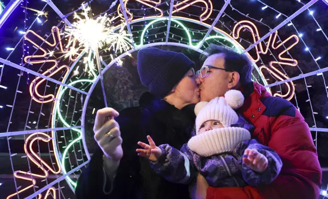 A couple share a tender moment as they walk with their child in a square decorated for Christmas and the New Year festivities in Donetsk in Russian-controlled Donetsk region, eastern Ukraine, Tuesday, Dec. 31, 2024. (AP Photo/Alexei Alexandrov)