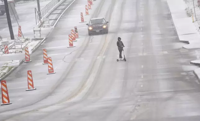 Snow falls as a car and a scooter make their way along a street Thursday, Jan. 9, 2025, in Dallas. (AP Photo/LM Otero)