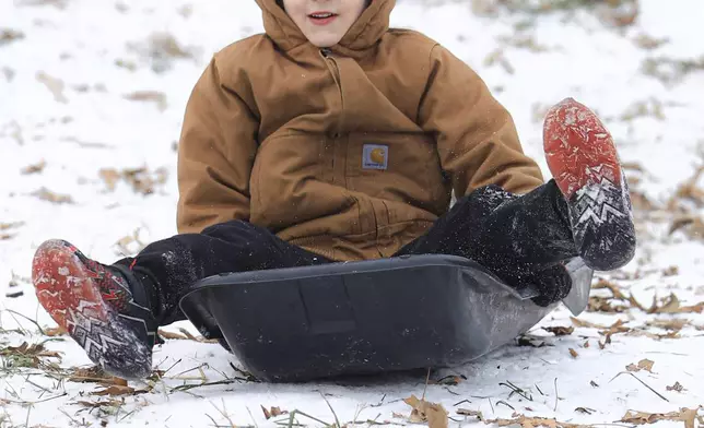 Taking advantage of the lingering ice and snow from the recent winter weather event, Dawson Mauro, 6, races down a steep hill behind Chautauqua Park while sledding, Wednesday, Jan. 8, 2025, in Owensboro, Ky. (Greg Eans/The Messenger-Inquirer via AP)