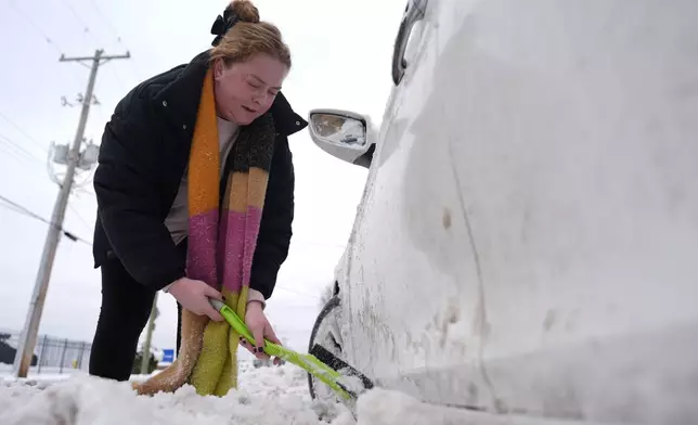 Taylor Mcilwain uses a snow brush to clear snow from around her car in Cincinnati, Tuesday, Jan. 7, 2025. (AP Photo/Carolyn Kaster)