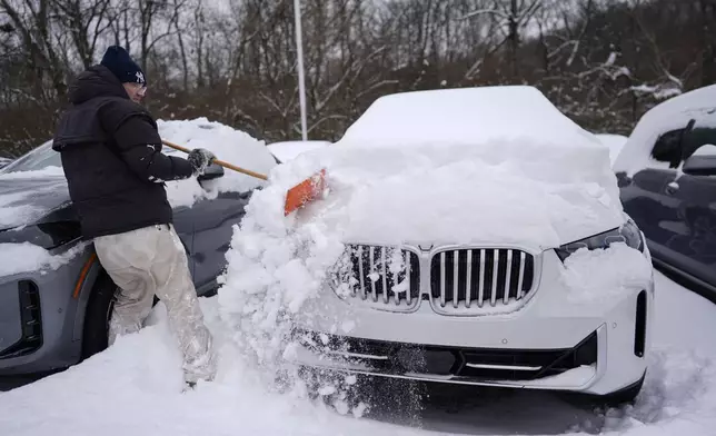 Cary Fallath, the BMW Store lot technician, clears snow from new cars in Silverton, Ohio, Tuesday, Jan. 7, 2025. (AP Photo/Carolyn Kaster)