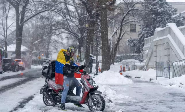 A man wearing a Venezuelan flag starts a moped as snow begins to fall again, Monday, Jan. 6, 2025, in Washington. (AP Photo/Jacquelyn Martin)