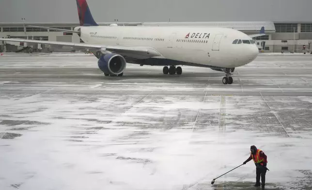 A worker clears snow from an apron before guiding a Delta Air Lines jet at the Detroit Metropolitan Wayne County Airport in Romulus, Mich., Monday, Jan. 6, 2025. (AP Photo/Charlie Riedel)